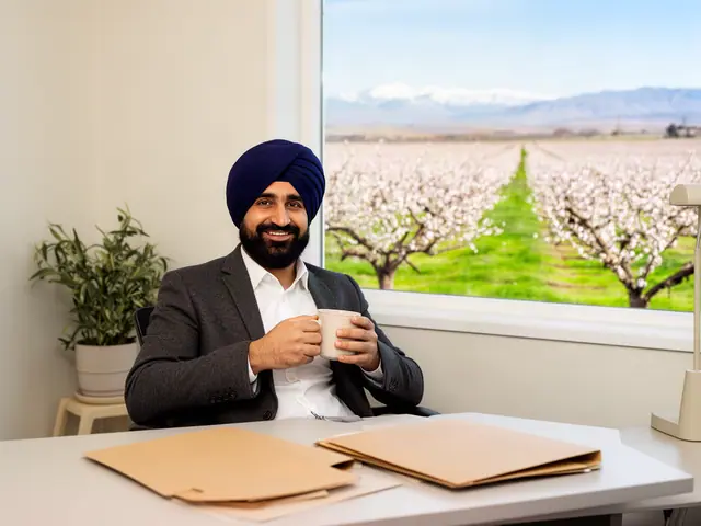 Smiling accountant in a navy turban and charcoal blazer holding a mug at a desk, almond orchard outside